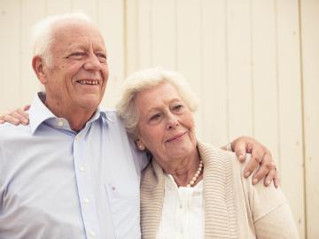 An eldery couple, woman resting her head on her husbands shoulder, looking in the distance