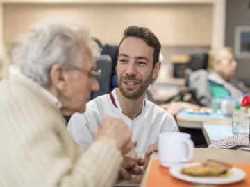 A nurse talking to an elderly man having breakfast