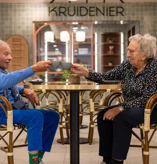 Deux résidents trinquant avec un café à une table du salon/bar de la résidence Boschart