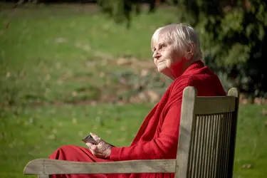 Résidente profitant du soleil assise sur un banc à la résidence Château Chenois dans le cadre du projet Living