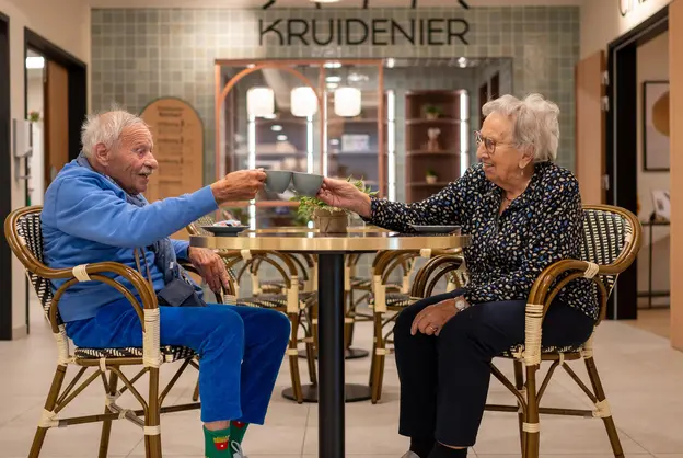 Deux résidents trinquant avec un café à une table du salon/bar de la résidence Boschart